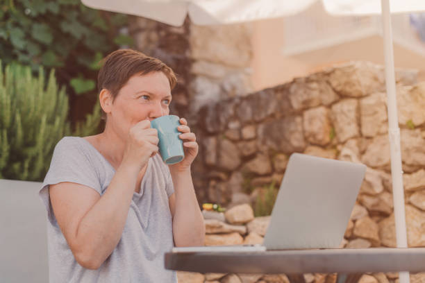 istock Woman drinking coffee while working from home terrace on laptop computer 1365182450