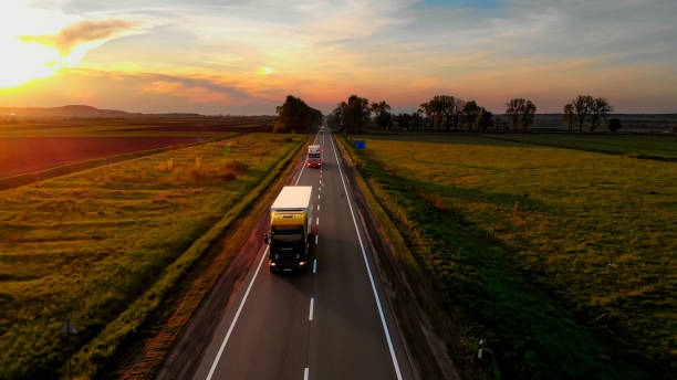 Amazing Aerial Drone View: Semi Trucks Delivering Goods by Road. Amazing Aerial Drone View: Semi Trucks Delivering Goods by Road. Sunset Summer time: Blue Sky, Red Sun.Sun Rays Shining the road. car transporter photos stock pictures, royalty-free photos & images
