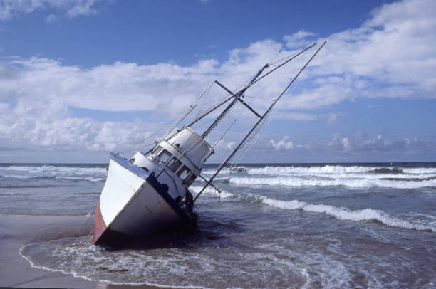 Boat Grounded In The Surf A fishing boat lists as it sits grounded in the surf. fishing boat sinking stock pictures, royalty-free photos & images