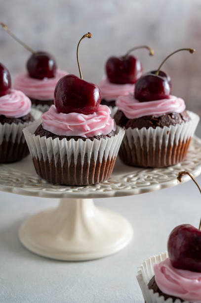 istock Chocolate cupcakes with fresh cherries and pink cream on cake stand. 1365188275