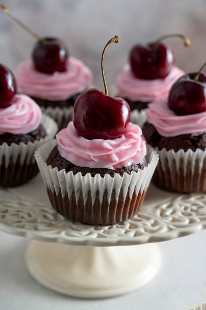 istock Chocolate cupcakes with fresh cherries and pink cream on cake stand. 1365188447