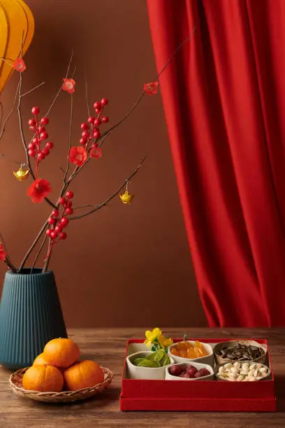 Vase with blooming branches next to box of nuts and candied fruits prepared for Chinese New Year celebration