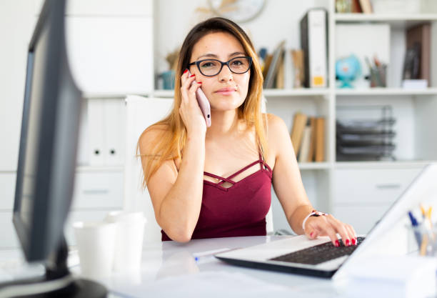 istock Woman using phone and working with laptop in office 1365190369