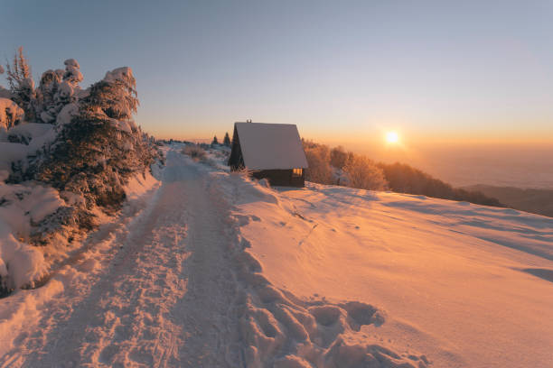 Log cabin covered with snow at sunset in mountains