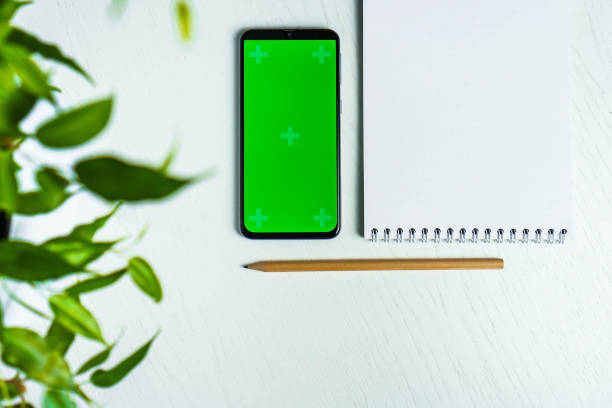 istock Green leave with blank notepad smartphone green screen mockup and pencil flat lay. Top view 1365193019
