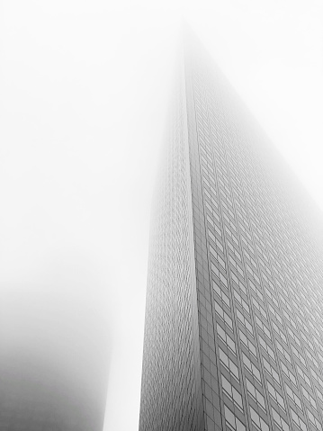 Low-angle shot of city skyscrapers vanishing upward into the fog