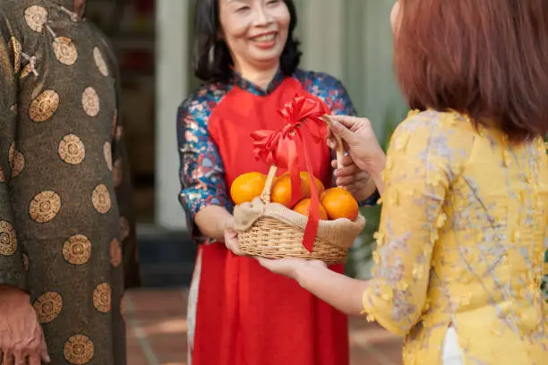 Woman giving decorated basket of mandarins to her senior parents for Tet celebration