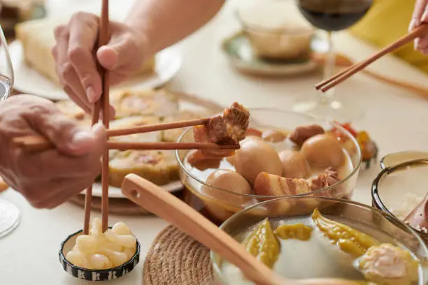 People with chopsticks taking braised pork, pickled garlic and other food from Tet dinner table