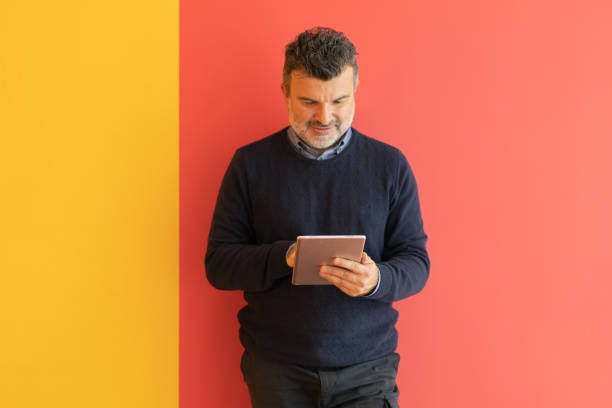 Handsome mature businessman holding digital tablet on colored background stock photo