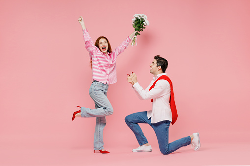 Full body side view young couple two friends woman man 20s in shirt making proposal give ring say yes isolated on plain pastel pink background Valentine's Day birthday holiday party engagement concept