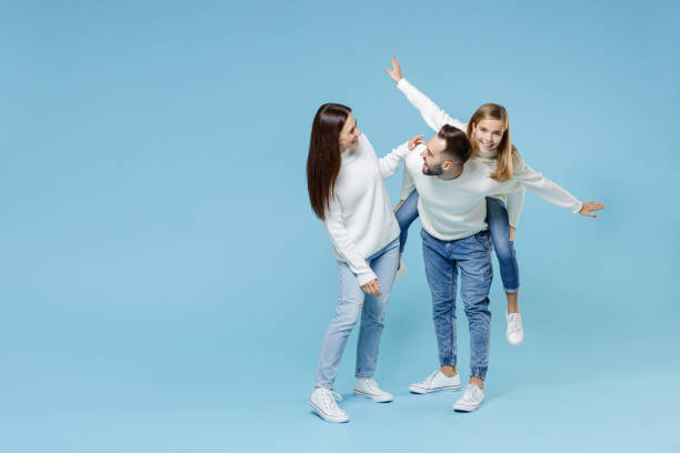 pleine longueur de jeunes parents souriants maman papa avec enfant enfant fille adolescente en pulls donnant un tour de cochon à joyeux, assis sur le dos isolé sur fond bleu. concept de parentage de jour en famille. - men fun father daughter photos et images de collection