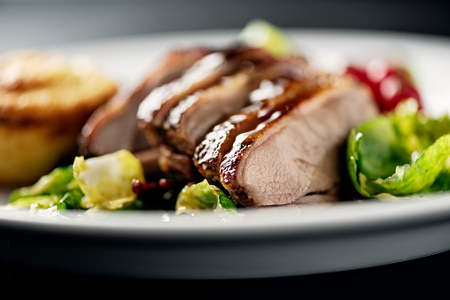Roasted duck breast with honey roasted sprout leaves and seasonal salad leaves and a red currant dressing. Colour, horizontal format with some copy space.