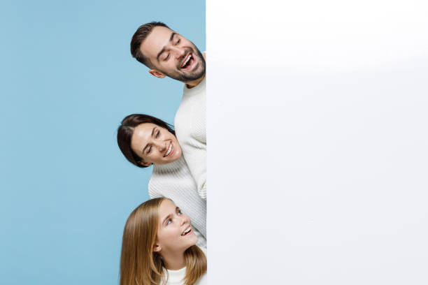 excited young parents mom dad with child kid daughter teen girl in sweaters hold big white empty blank billboard mock up copy space isolated on blue background studio. family day parenthood concept. - child women outdoors mother imagens e fotografias de stock