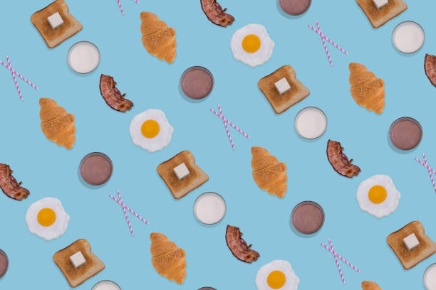 istock Creative pattern made with fried eggs, slices of crispy bacon, toast bread, croissant and glasses of milk on blue background. 1365207661