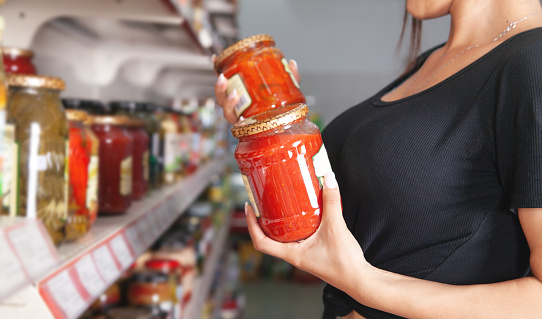 Woman chooses tomato paste at supermarket.