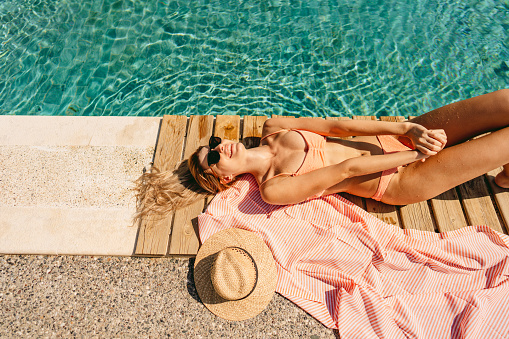 Photo of a young woman sunbathing by the pool.