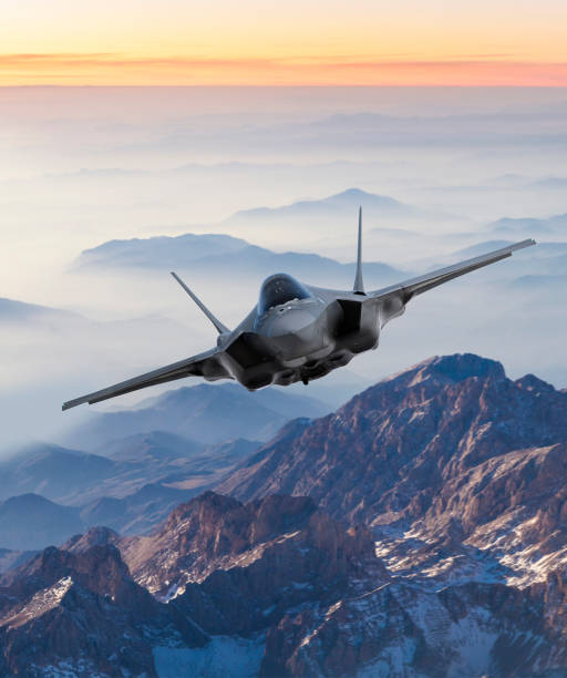 Fighter Jet flying over mountains at sunset stock photo