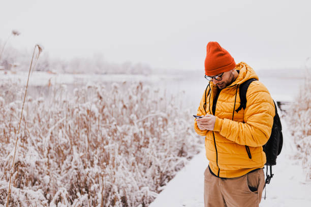 istock Young man using smartphone in nature on a snowy day 1365212531