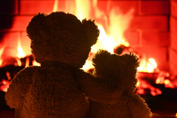 two teddy bears are sitting hugging and looking at the fireplace flame. Valentine's Day, Friendship Day, Childhood