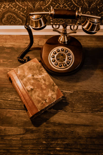 An old Rotary phone with brass details on dark wood table with brown leatherbound book