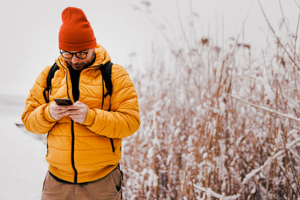 istock Young man using smartphone in nature on a snowy day 1365213759
