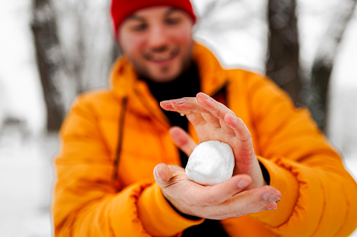 View of Young Handsome Man in Warm Clothing Throwing a Snowball During a Winter Day
