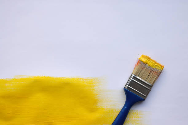An artist paints wooden boards with a brush with synthetic bristles with acrylic yellow paint close-up