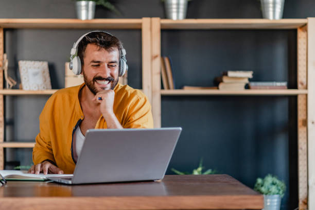 istock Young man with headphones is working from home on laptop 1365216993