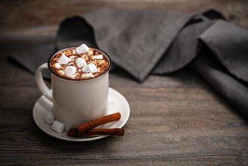 Mug of hot chocolate with marshmallow and cinnamon on a wooden table