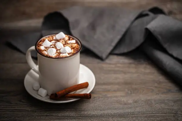Photo of Mug of hot chocolate with marshmallow and cinnamon on a wooden table
