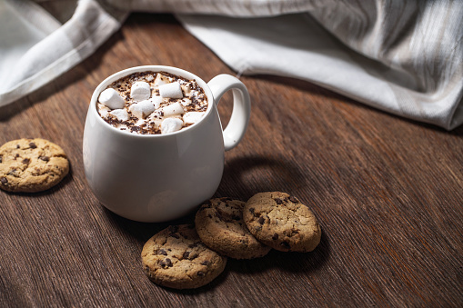 Mug of hot chocolate with marshmallow and cookies on a wooden table
