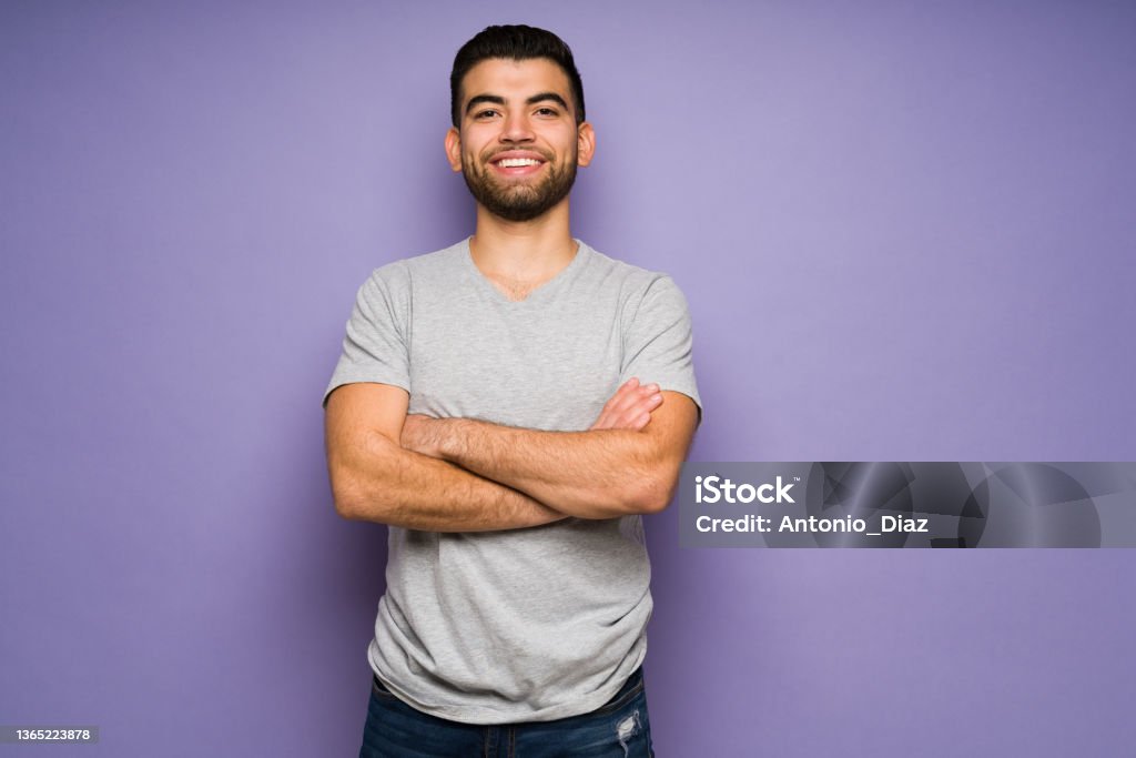 Attractive man feeling cheerful Handsome hispanic young man with casual clothes feeling confident and smiling in front of a purple studio background Men Stock Photo