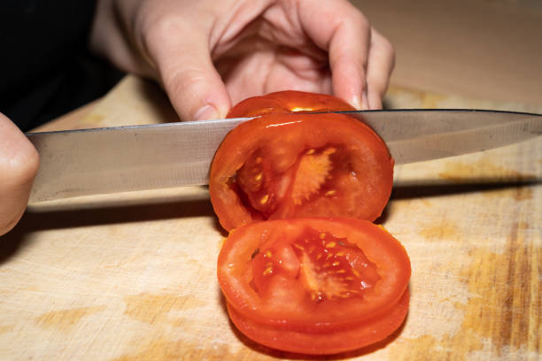 istock Woman cuts a tomato into slices on a wooden board 1365227497