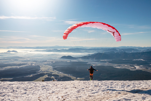 Paragliding in mountains, winter snow and red parachute.