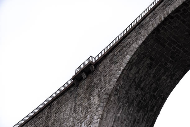 Architectural detail in close-up view from below of arches and columns pillars of stone brick railway bridge against high key lighting sky in Chamonix France.