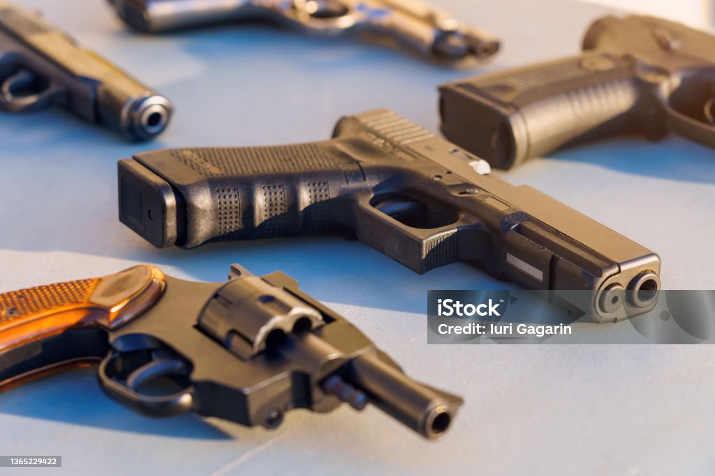 A gun on the table among the weapons, selective focus. Crime news background. A gun on the table among the weapons, selective focus. Crime news background. The concept of rules for the owners of firearms. Shooting training. Confiscation of contraband and illegal carrying. Gun Stock Photo