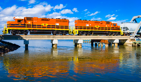 Fernandina Beach, Florida, USA-December 28, 2021-A yellow and orange First Coast Railroad engine is reflected in the waters of Kingsley Creek as it crosses the swing bridge in  Fernandina Beach, Florida