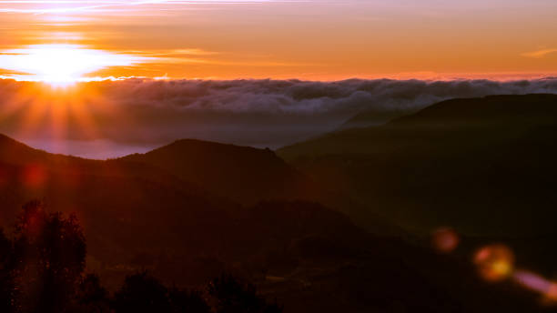istock Orange shining sun rising over the clouds on a mountain range landscape 1365232809