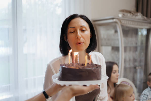 Family celebrating birthday with a cake A cheerful family celebrating birthday at home, at the table in the living room holding a cake, woman blowing candles woman birthday cake stock pictures, royalty-free photos & images