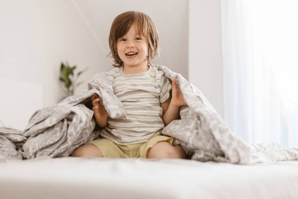 4 세의 귀여운 소년이 뛰어 침대에 탐닉하고 담요에 자신을 감싸. 아이들과 함께 재미있는 홈 게임 - portrait germany party bed 뉴스 사진 이미지
