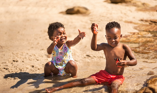 Cute little kids sitting in water on the beach and playing with toys on a summer day