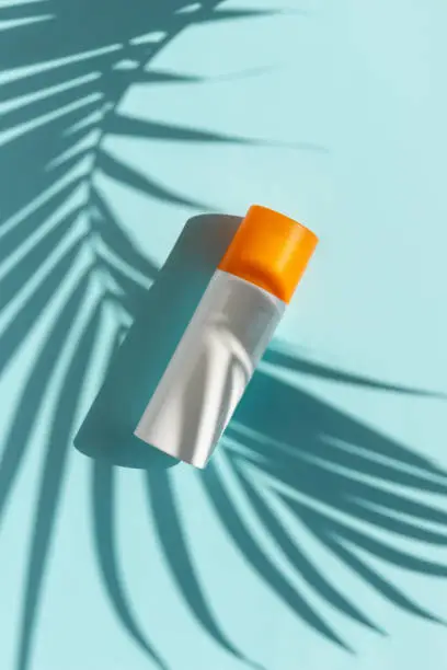 Bottle of sunscreen with palm leaf shadow on blue background. Summer body care beauty treatment concept. Creative composition in minimal style