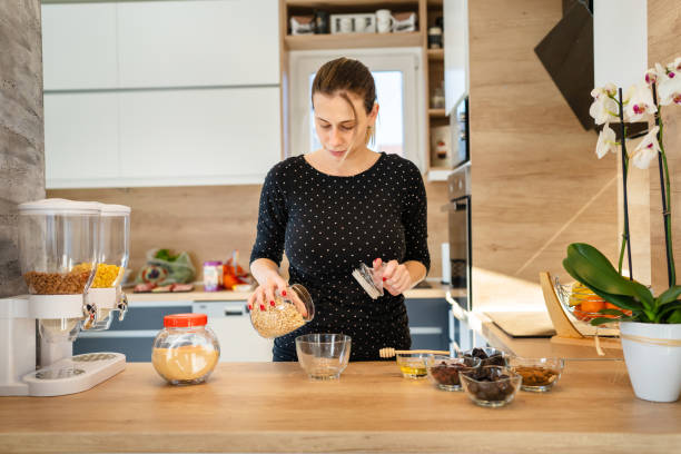 istock One young caucasian woman standing in the kitchen making healthy breakfast front view millennial female adult putting oatmeal oatflakes in the bowl preparing meal real people copy space 1365241533