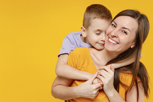 Happy young woman have fun with cute child baby boy 5-6-7 years old in violet t-shirt. Mommy little kid son posing together hugs isolated on yellow background studio. Mother's Day love family concept