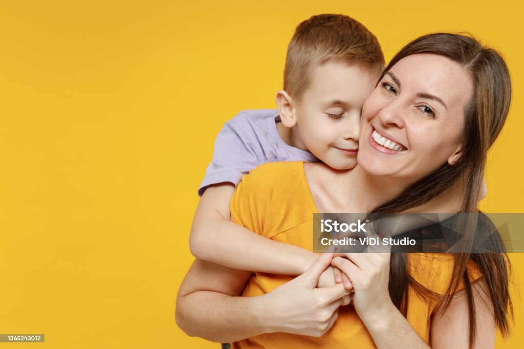 Happy young woman have fun with cute child baby boy 5-6-7 years old in violet t-shirt. Mommy little kid son posing together hugs isolated on yellow background studio. Mother's Day love family concept. Happy young woman have fun with cute child baby boy 5-6-7 years old in violet t-shirt. Mommy little kid son posing together hugs isolated on yellow background studio. Mother's Day love family concept Mother Stock Photo