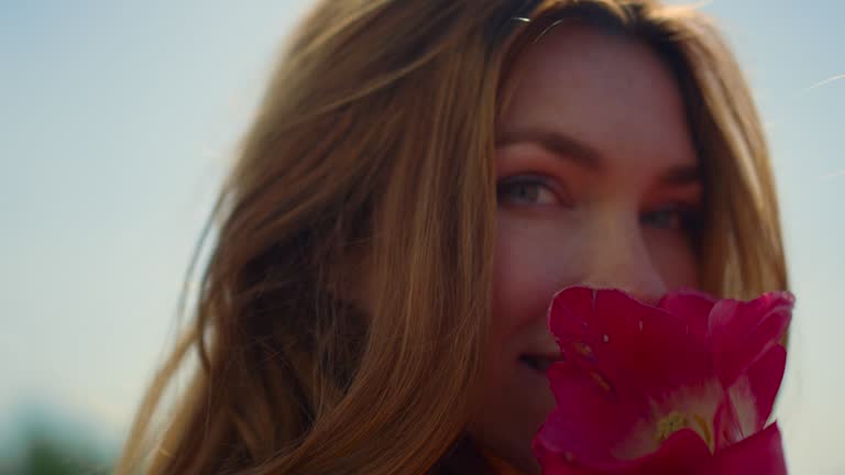 Closeup beautiful woman face enjoying tulip flower in soft sunset light outdoor.