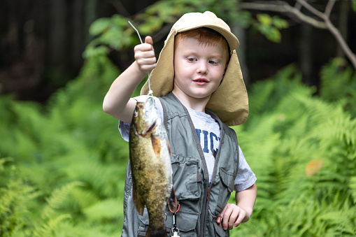 Cute Redhead Boy Showing his Catch of the day after fishing. He is holding his fish in the air and smiling as he is very proud. It is summer season in Quebec.