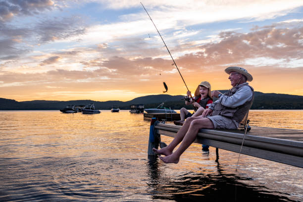 grand-père et petit-fils pêchant au coucher du soleil en été - fishing lake grandfather grandson photos et images de collection