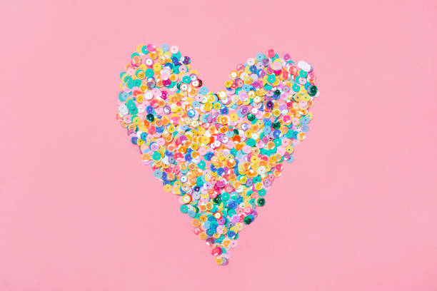istock Heart made of multicolored sequins confetti on pink background. Flat festive composition copy space 1365253287