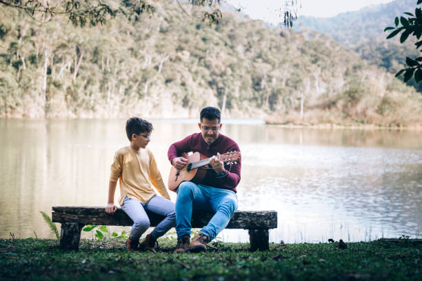 Father and son playing acoustic guitar by the lake Father and son playing acoustic guitar by the lake father and son guitar stock pictures, royalty-free photos & images